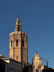 Close-up view of the cathedral bell tower in Valencia, Spain, standing tall under a bright blue sky.