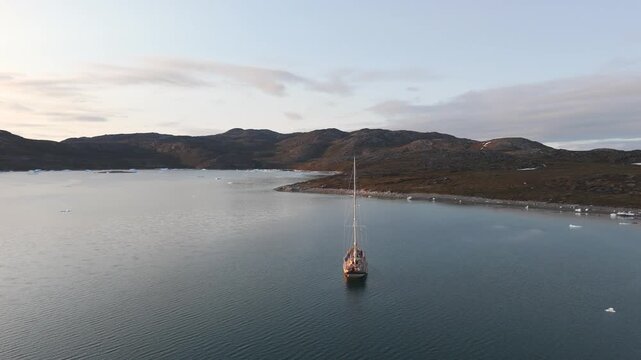 Drone circles solitary boat near Greenland coast amid ice floes and midnight sun