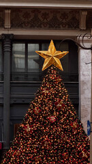 Tall festive Christmas tree with red ornaments and golden star, placed in a city square in Rome during holidays.