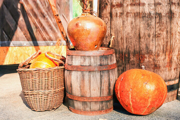 Orange pumpkins in wicker basket, old wooden barrel, rustic clay vase in autumn yard