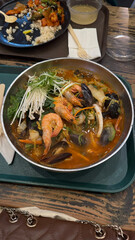 Hot bowl of Korean seafood noodle soup with shrimp, mussels, and vegetables in spicy broth, served on a food tray.