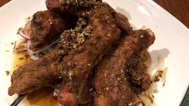 Close up of deep fried pork ribs with spices on a white plate in a restaurant.