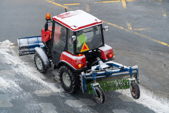 A tractor with a brush clears the road from snow. Repair, cleaning of roads in winter. City improvement services in the cold season. A snowplow cleans the sidewalks. A snowplow clears streets of snow.