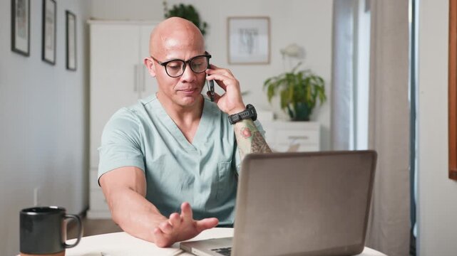 Bald Doctor Consults Remotely on Phone While Using Laptop in a Bright Home Office