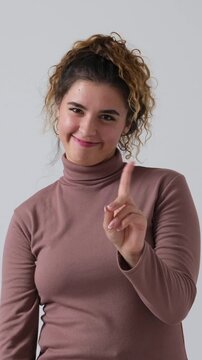 A young woman with curly hair smiles and wags her index finger in a gesture of denial or warning. Isolated on a white background. Vertical video.