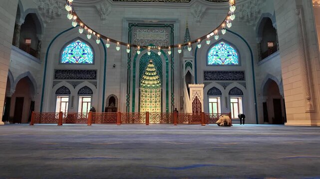 Interior view of Barbaros Hayrettin Pasa Mosque in Levent, Istanbul. A man praying in front of the ornate Mihrab with turquoise tile patterns and hanging ring chandelier. Islamic architecture in Turke