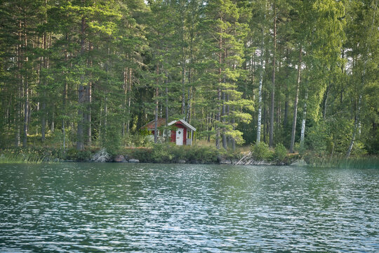 Red wooden house on the Swedish lake with forest reflection in natural scenery.