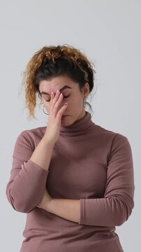 Frustrated young woman rolling her eyes, crossing her arms, and doing a facepalm gesture, isolated on a white background. Vertical video.