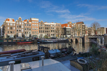 Scenic view of the historic Oudeschans canal in Amsterdam featuring traditional Dutch gable houses and houseboats under a clear blue sky.