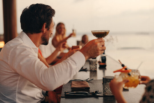 Group of friends enjoying a sunset dinner with drinks at a beachfront venue
