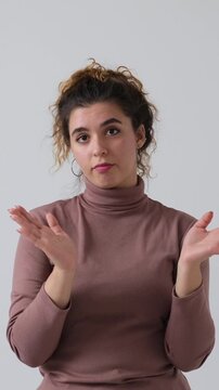A young woman sarcastically claps her hands and crosses her arms with a look of disapproval, isolated on a white background. Vertical video.