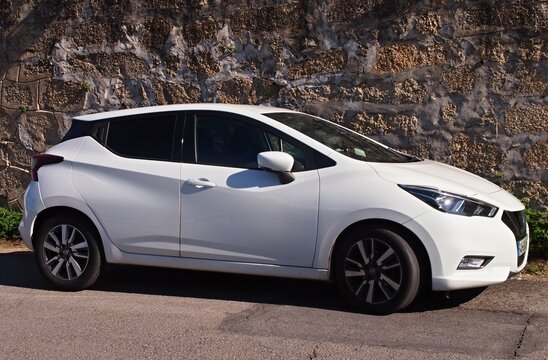 White Nissan Micra subcompact car parking by stone wall