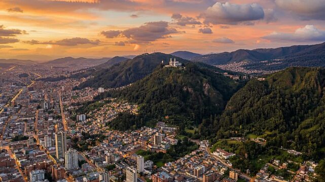 Vibrant Cityscape Panorama of Bogota Colombia at Golden Hour Dusk with Lush Green Monserrate Hillside and Dramatic Sunset Sky Above Dense