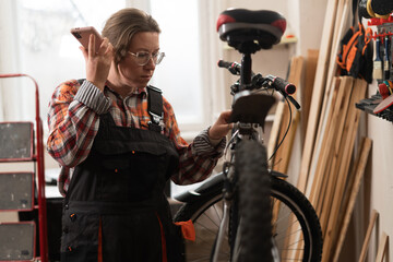 Focused bicycle mechanic listening voice message while repairing bicycle in workshop.