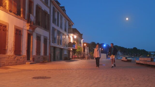 Couple Walking Along The Cobbled Quays Of Saint-Goustan Historic Port At Dusk In Auray, Brittany, France. Static Shot