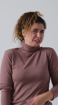 A disgusted young woman expresses aversion and fear, covering her face in horror. Vertical video isolated on a white background.