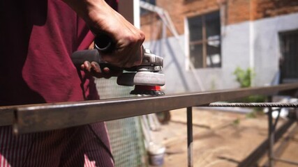 Male hands of professional mechanic holding special instrument and clearing metal construction from rust outdoor. Arms of young worker grinding iron detail with electric circular saw tool. Close up