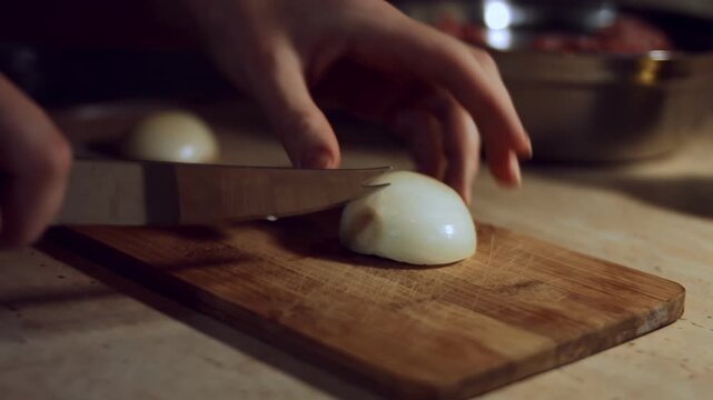 Hands cutting half of the onion into cubes ona wooden board