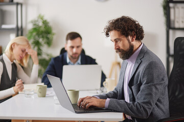 Obraz premium Group sits around a table in a modern office. They discuss ideas while one member types on a laptop. Focus is on teamwork and planning for future projects.