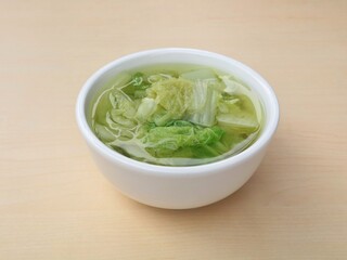 Fresh chinese cabbage soup in a white bowl on wooden table with high angle view. perfect for diet, wellness, and asian cuisine concepts