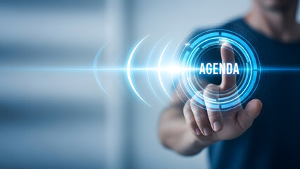 Man's finger touching a glowing blue circular button labeled AGENDA on a futuristic interface
