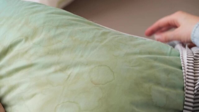 Female hands removing pillowcase from pillow in a living room. Dirty stains sweat or saliva on a green pillow. Conscious home care and sustainable living concept. top view. High quality 4k footage