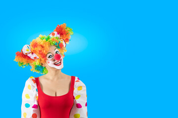 Funny female clown, woman entertainer dressed as a colorful Joker in a suit and wig, with clown whiteface makeup