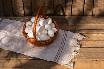 Chicken eggs in a wicker basket with wall of chicken coop, barn or wooden grunge fence in the background. Countryside outdoor setting