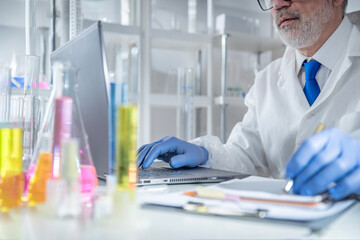 Experienced professor recording experimental data on a laptop while working in a laboratory. Concept of digital research documentation, data analysis, academic standards and modern scientific workflow