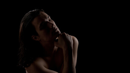Male portrait resting chin on hand in low light studio. Concept of skincare routine, self care reflection, mental wellness, emotional balance, and modern male lifestyle.