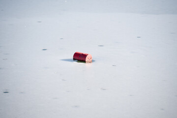 A red navigation buoy frozen into a smooth, pale ice surface. The buoy serves as a water safety and...