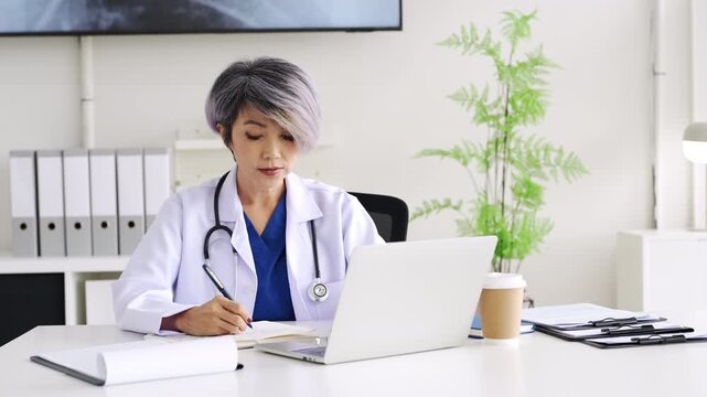 Doctor looking at laptop screen writing in notebook for research planning or medical tech innovation in hospital office. Healthcare medic worker, research strategy book notes and online communication.
