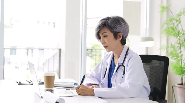 Doctor looking at laptop screen writing in notebook for research planning or medical tech innovation in hospital office. Healthcare medic worker, research strategy book notes and online communication.