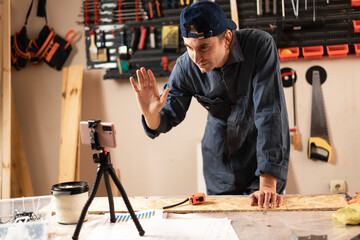 My DIY video. carpenter recording tutorial wooden masterpiece waving hand on his followers working in workshop.