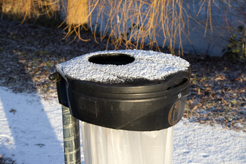 Black public trash bin with plastic bag covered in white frost and snow