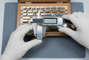 Gloved hands measuring gauge block with digital caliper