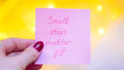 Hand holding pink sticky note with motivational quote and soft background