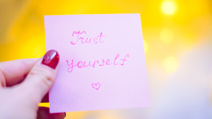 Hand holding pink sticky note with motivational message and soft background