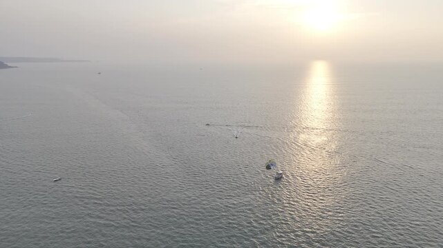 Sunset view of Mobor Beach in South Goa during winter, featuring parasailing boat and fishing boats on the Arabian Sea, with golden sunlight reflecting on calm water under a warm evening sky.