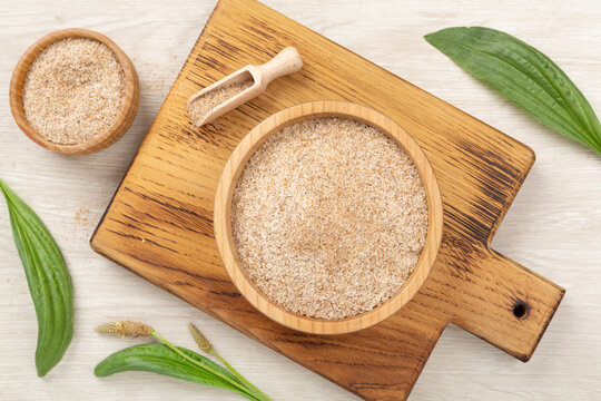 Psyllium husk powder with fresh leaves on wooden background, top view