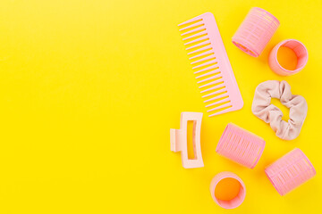 Pink hair curlers and brush on color background, top view