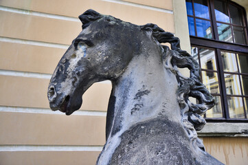 Zbliżenie zniszczonej rzeźby konia na tle beżowego okna fasady budynku. © Pol Badger