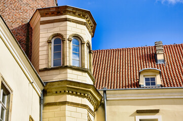 Zabytkowy beżowy budynek z wieżyczkami i czerwonym dachem pod jasnoniebieskim niebem - detal architektoniczny - Zamek Piastów w Legnicy. © Pol Badger