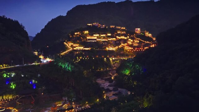 Aerial shot of illuminated traditional village buildings on mountain slope at night. The famous Wangxiang Valley Scenic Area is located in Jiangxi, China.