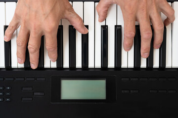 Closeup of male musician playing on digital synthesizer at home. Overhead view of hands playing electronic keyboard, home practice.