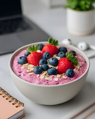 Healthy smoothie bowl topped with berries and oats on a modern desk.