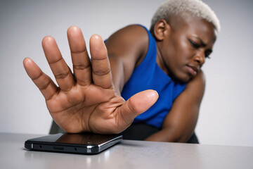 Angry plus size Black woman in bright blue top pushing smartphone away