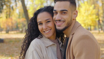 Fototapeta premium Close-up hispanic couple in love looking at camera in autumn park city portrait touching faces cheeks smiling enjoying love Arabian guy and girl happy smile married family man woman multiethnic lovers