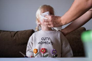 Mom caring for sick child suffering from flu or allergy, cleaning nose with handkerchief.