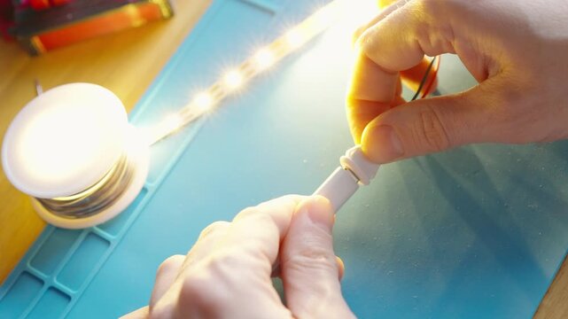 Top view close-up of hands connecting a USB Type-C cable to a soldered Type-C port on an LED strip, lighting up on a silicone mat, DIY electronics hobby project